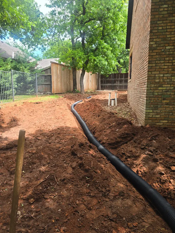 Corrugated drain pipe laid in an open trench along a backyard fence line