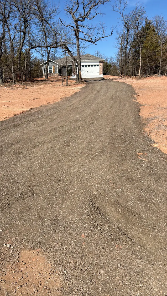 Fresh gravel drive climbing through winter oaks to a detached garage