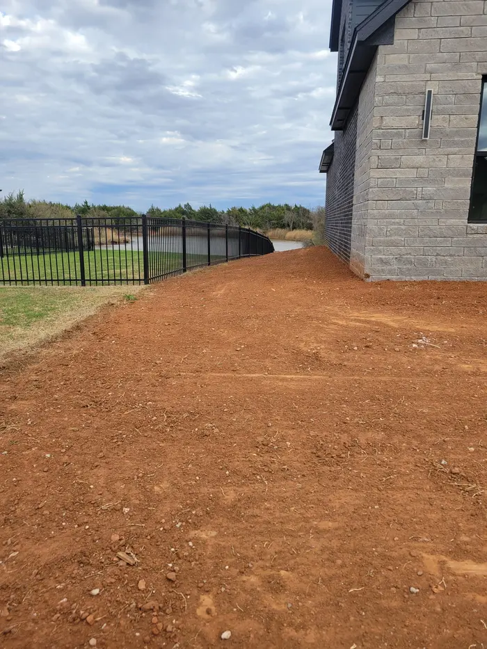 Smooth finish grade along a stone home's side yard toward the iron pond fence