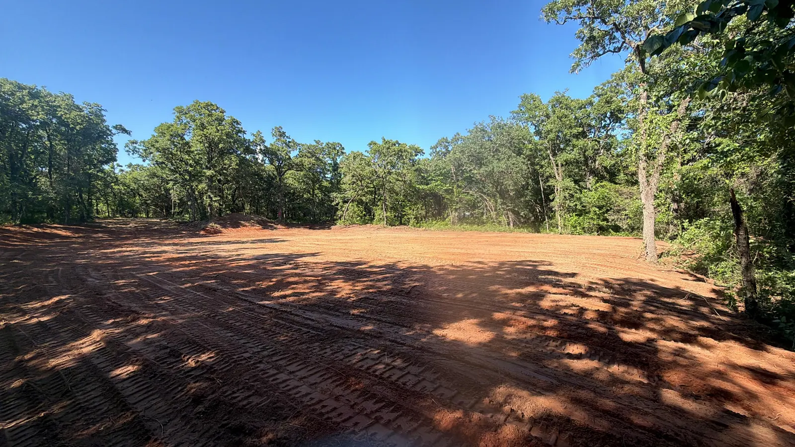 Finished cleared and graded pad in a woodland clearing under a deep blue sky
